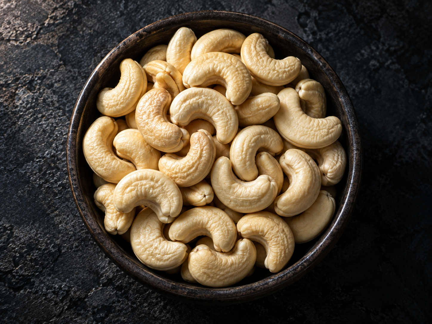 Raw whole cashew kernels in a dark bowl