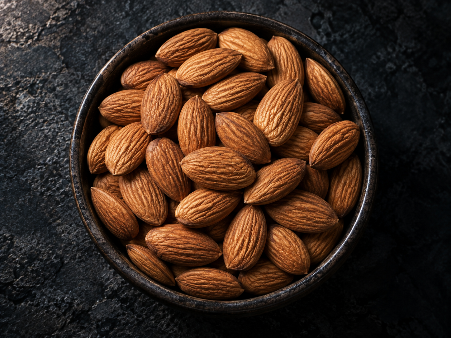 Whole almonds with brown skin in a dark bowl